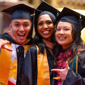 Three students wearing graduation regalia pose for a picture in Saint Ignatius church
