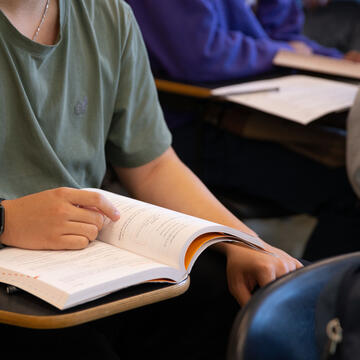 Torso and arms of student sitting at a desk with one hand on an open book