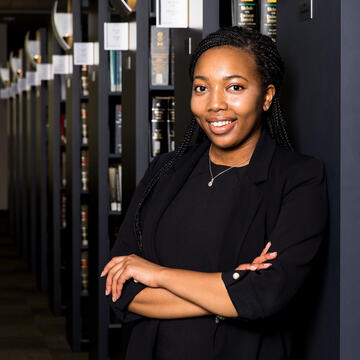 Student poses with crossed arms against a bookshelf.