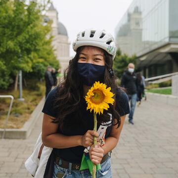 Student with a bike helmet on holds a sunflower.