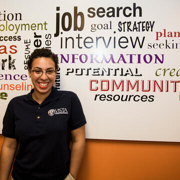 Americorps Vista participant stands is front of word cloud board