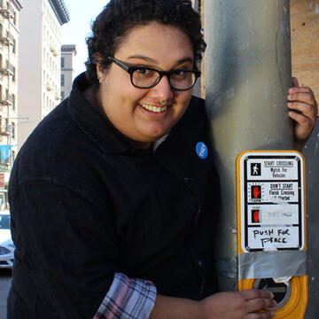 Student pushes a street crossing button that reads Push for Peace.