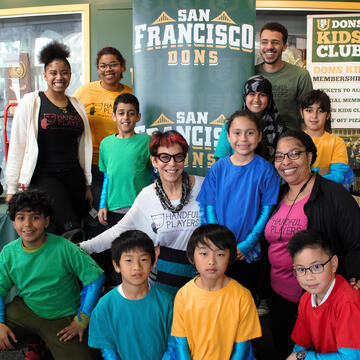 Adults and children pose in front San Francisco Dons sign