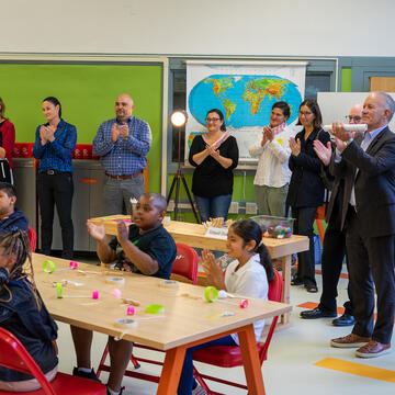 Group of adults stand and applaud while children sit at a table