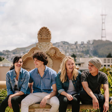 Four students sit on a bench with a view of campus in the background.