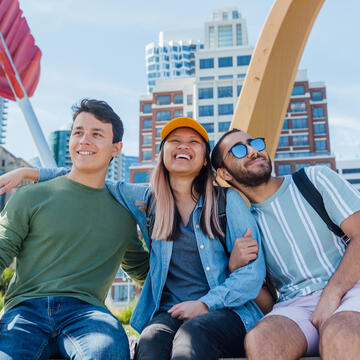 Three students embrace in front of a bow and arrow sculpture in San Francisco.