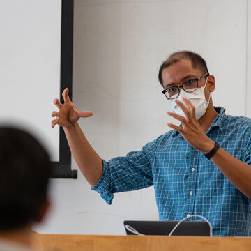 Professor gesturing with both hands lectures at a podium