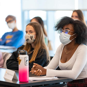 Students with name tags on the table sit in two rows and listen