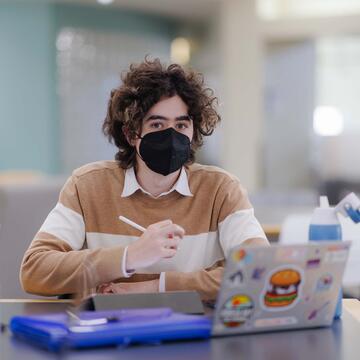 Student sits at a desk with a tablet and a laptop in front of them