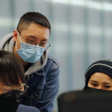 Three students gather around a screen in a computer lab