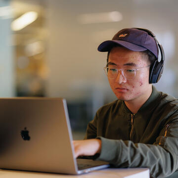 Student with headphones on studies on a laptop.