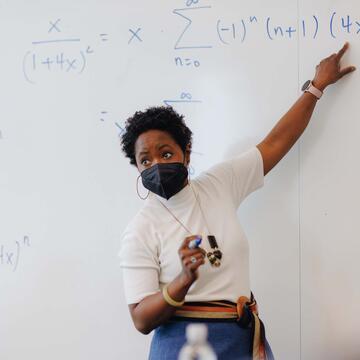 Instructor points to a part of a math formula on the white board
