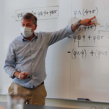Instructor points to a part of a math formula on the white board