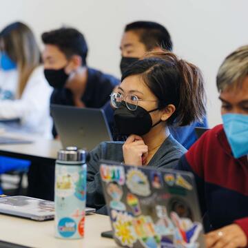 Student with a closed laptop sits and listens attentively with their hand under their chin while surrounded by other students