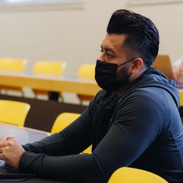 Student with a laptop and a can of drink next to it listens in lecture hall