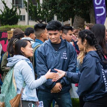 Three students standing together, two of them shaking hands