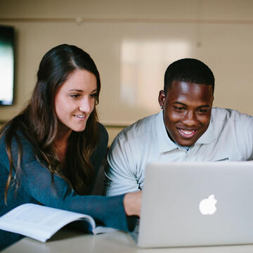 Three students study around a laptop.