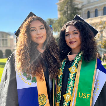 Two graduates in regalia pose on the grass