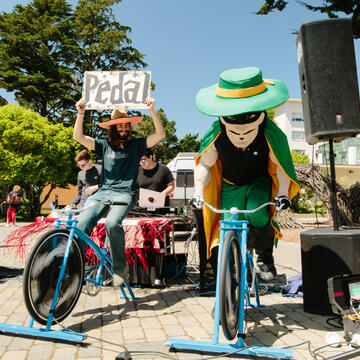 Student and USF mascot pedal stationary bikes at fair