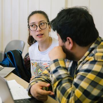 Two students sit as desk and discuss