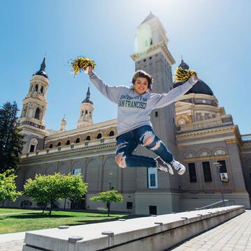 Student jumps in the air in front of St. Ignatius Church holding pom poms