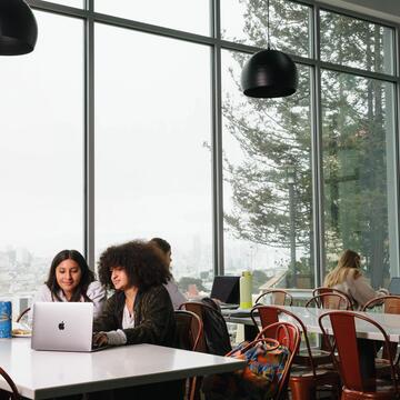 Two students sit at table with laptop in front of large window at Koret Lodge