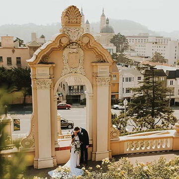 Paris Blatecky and their spouse kissing in their wedding attire on the Lone Mountain steps.