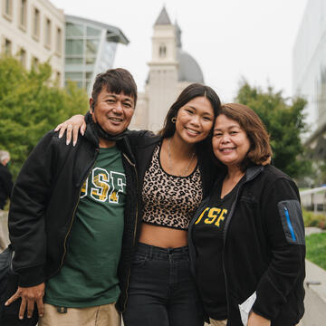 New student poses on campus hugging parents.