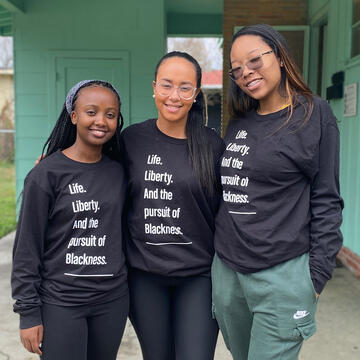 Three students pose together, all wear shirts that read "Life. Liberty. And the pursuit of Blackness."