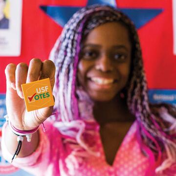Student smiles and holds a button that says USF Votes.