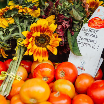 Basket of tomatoes and flowers with sign that says "$3.50 lb, big beef steak tomatoes organic!" 