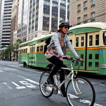 Person biking in Downtown San Francisco with a trolley behind them.