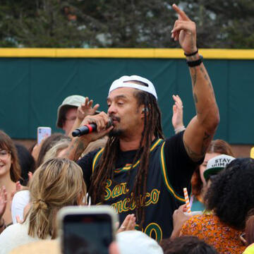 Michael Franti on the mic walks through the crowd, wearing a USF basketball jersey
