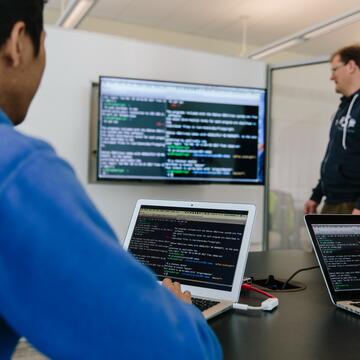 Student and professor looking at code on a computer screen.