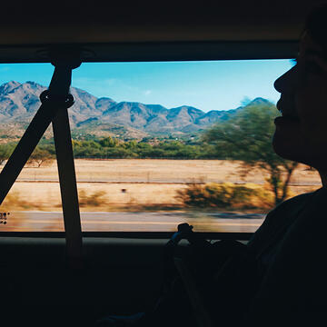 Car passenger silhouetted in shadow with passing mountains and desert landscape framed by window 