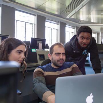 Three students looking at a laptop in a computer lab.