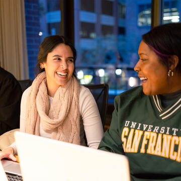 Two USF students chatting while working at their laptops