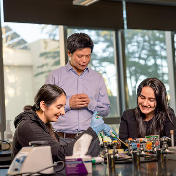 professor looks on as two students work with lab equipment