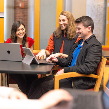 three students gathered around a table laughing together