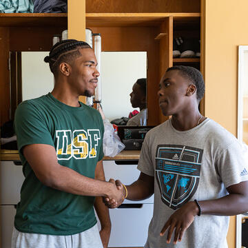 two students shake hands inside dorm