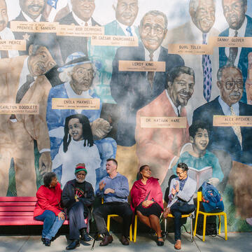 group of people sitting on a bench in front of a mural