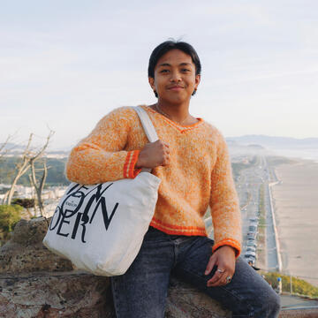 Student sits on a cliff above the beach.