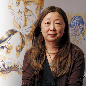 Eileen Fung sits in front of a mural with faces on it.