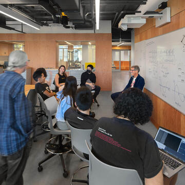 Group of students conversing next to a whiteboard.