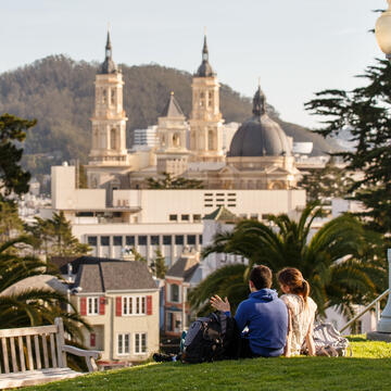 Two students sit on the lawn on a hill overlooking campus