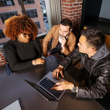 three graduate students overlooking laptop at usf downtown campus