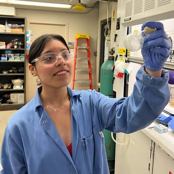 student in lab coat holds examines equipment