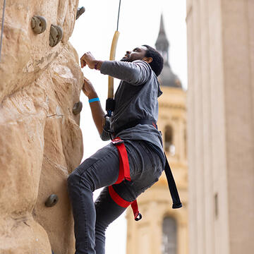 student moving up rock climbing wall