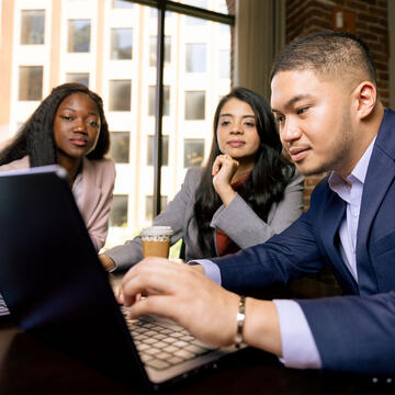 Students in business look at a laptop around a table