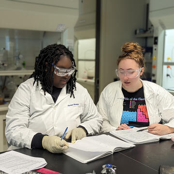 two students in lab coats looking at research